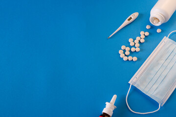 Medicine and health concept. Pills, thermometer and medical mask on a blue background. Place for your text.