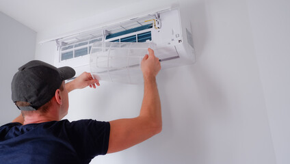 Air conditioner repair and maintenance. The technician removes the filter of the indoor unit for cleaning.