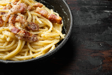 Traditional italian dish spaghetti carbonara with bacon in a cream sauce, in cast iron frying pan, on old dark  wooden table , with copy space for text