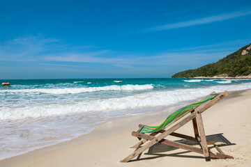 Green Deck chair at the tropical sandy beach with blue wave and clear sky in summer time