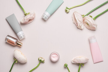 Cosmetics for face and body on pink pastel background with ranuculus flowers. Beauty products. Frame background