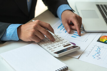 businessman or accountant hand working on calculator to calculate financial data report, accounting document and laptop computer at office, business concept