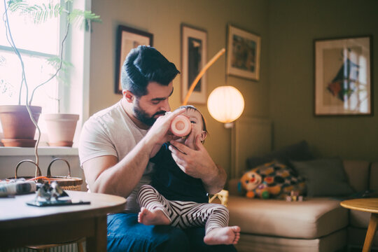 Father feeding baby girl from bottle in living room at home