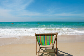 Green Deck chair at the tropical sandy beach with blue wave and clear sky in summer time