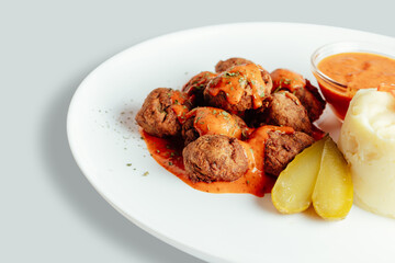 Meatballs with tomato sauces, mashed potatoes and pickles.