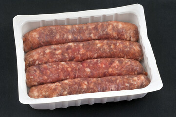 Barquette en plastique de saucisses de porc crues en gros plan sur fond noir