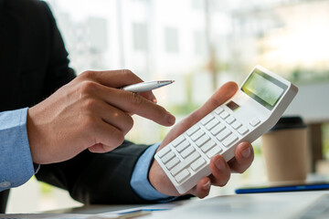 businessman or accountant hand working on calculator to calculate financial data report, accounting document and laptop computer at office, business concept