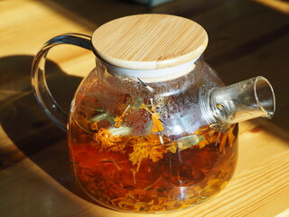 Herbal medicinal tea with dried flowers of marigolds and calendula. Glass teapot with brewed tea in the evening light.