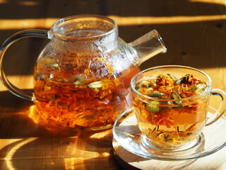 Glass teapot and glass with brewed tea in the evening light. Herbal medicinal tea with dried...