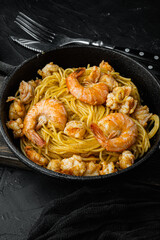 Seafood spaghetti pesto ready to eat, in cast iron frying pan, on black stone background