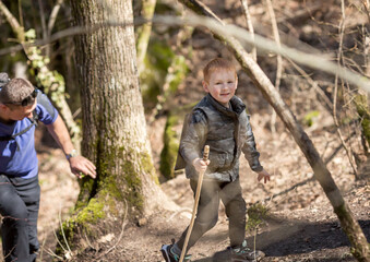 dad and son go uphill in the forest on a hike, the child is happ