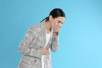 Woman in office suit suffering from stomach ache and nausea on light blue background, space for...