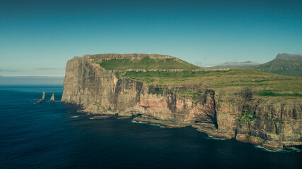 Panoramic view on coastline of island Eysturoy with rock formations Risin og Kellingin on Faroe Islands during the day with sun and blue sky, blue ocean and green cliffs.