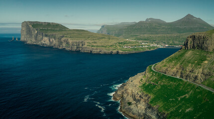 Panoramic view on coastline of island Eysturoy with rock formations Risin og Kellingin on Faroe Islands during the day with sun and blue sky, blue ocean and green cliffs.