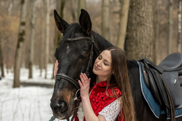 Obraz premium beautiful woman in white dress and red cape with black horse in spring forest 
