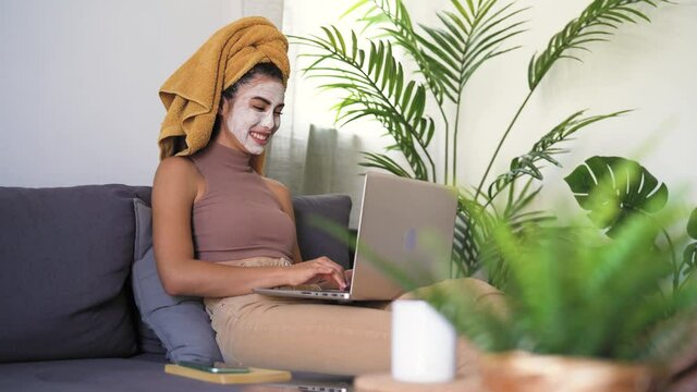 Young woman using laptop while having skin care day at home 