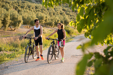 A couple of triathletes push the bike and rest after training while having a conversation