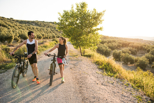 A couple of triathletes push the bike and rest after training while having a conversation