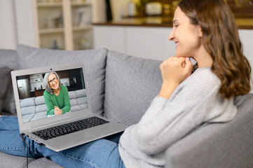 Side view glad young woman using a laptop computer for video connection with an elderly female on...