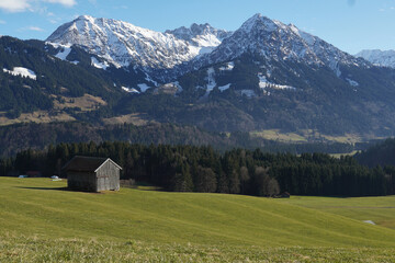Fototapeta na wymiar Winteruntypisches Bergpanorama in den Allgäuer Alpen mit grünen Talflanken und Schnee nur auf den Gipfeln
