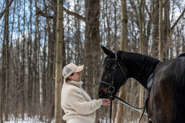 Obraz premium beautiful woman in brown cap and jacket with black horse in spring forest 