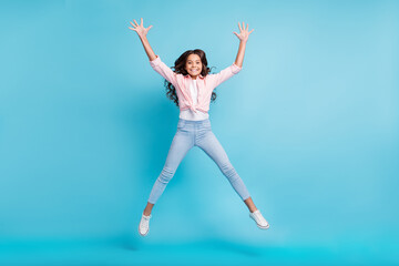 Fototapeta na wymiar Full body portrait of carefree school girl jumping raise hands have fun isolated on blue color background