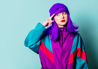 Surprised white girl with purple hair and 80s tracksuit point finger on her head on blue background