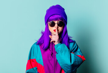 Stylish white girl with purple hair, 80s tracksuit and sunglasses show quiet gesture on blue...