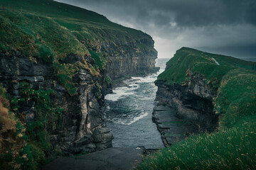 In the gorge in the village of Gjogv on Eysturoy, ocean and steep cliffs of the canyon, dark cloudy...