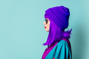 Stylish white girl with purple hair, 80s tracksuit and sunglasses on blue background