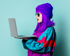 Stylish white girl with purple hair and 80s tracksuit with laptop on blue background