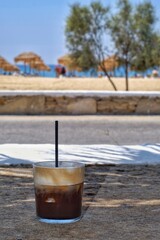 Closeup view of an iced greek  coffee, also known as freddo cappuccino with a straw at a beach in...