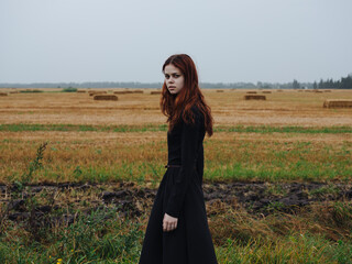 Beautiful woman in a black dress with red hair and a dry field in the background