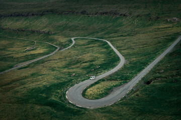 White campervan on a scenic winding pass road in grassland on Faroe Islands.