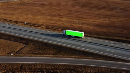 Truck with green screen on trailer drives along the highway in the rays of the setting sun. Mockup concept for adding your logo, slogan or company name.  Cargo transportation, international trade.