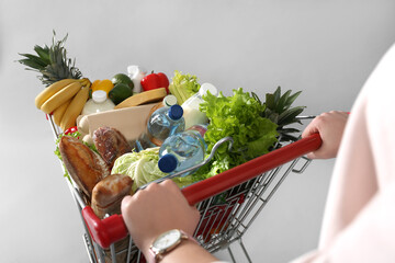 Woman with shopping cart full of groceries on grey background, closeup