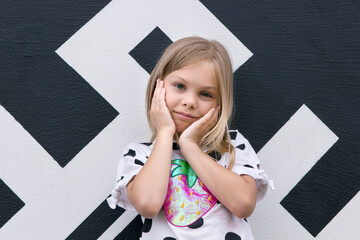 A child girl six seven years old against the background of a city wall with graffiti. The child is...