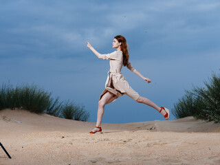 A woman in a beige dress walks with a long stride on the beach