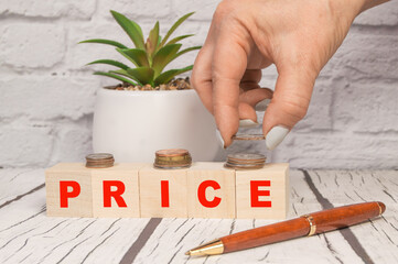 The concept of price, money, finance or savings by using a cubic wooden block with letters, the hand folds the coins on a light wooden table