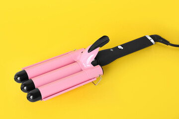 Modern triple curling iron on yellow background