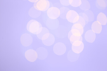 Blurred view of festive lights on lilac background. Bokeh effect