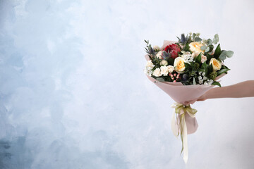 Woman with bouquet of beautiful roses on light blue background, closeup. Space for text