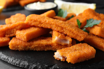 Tasty fresh fish fingers on black slate plate, closeup