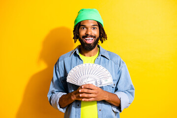 Photo of young happy excited crazy smiling cheerful afro man hold lot of money dollars isolated on yellow color background