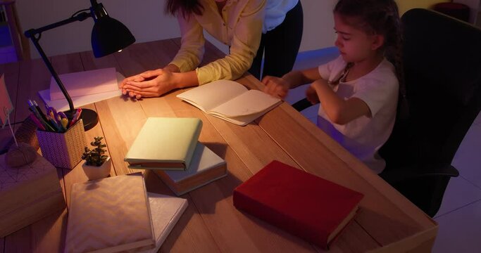 Angry mother scolding her little daughter for mistake in homework late in evening