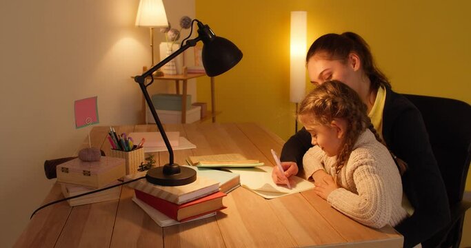 Woman helping her little daughter with homework late in evening