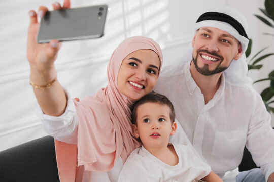 Happy Muslim family taking selfie on sofa at home