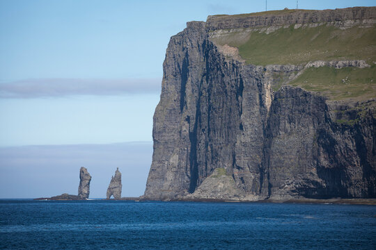 Risin og Kellingin rocks on Faroe Islands during the day with sun and blue sky, ocean in the front.
