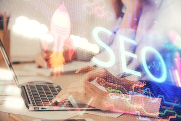 Double exposure of woman hands working on computer and seo hologram drawing. internet search...