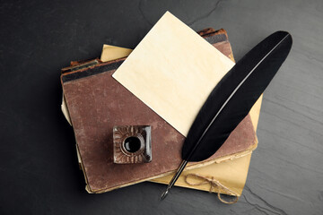 Feather pen, inkwell and old books on black table, top view - obrazy, fototapety, plakaty